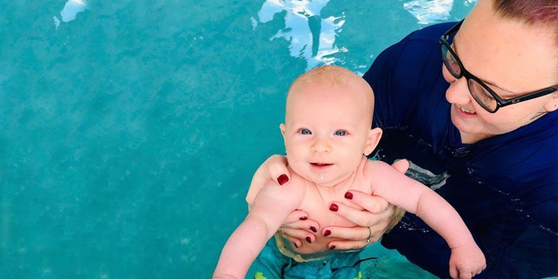 Parent holding a smiling young baby in a swimming class