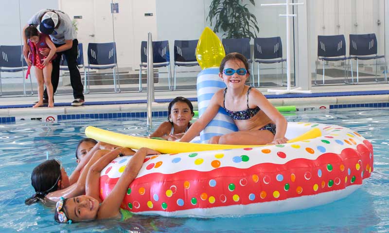 Five kids in a pool having fun with a big birthday party swim float