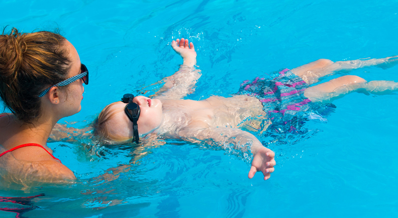 A young boy learning to float on his back in a pool