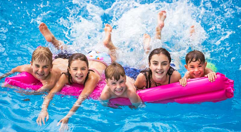 Five kids on a raft in a pool kicking and splashing