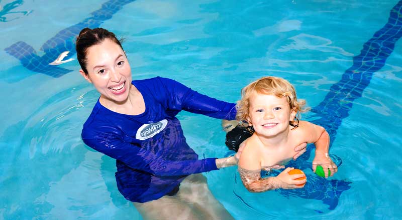 Smiling young toddler boy and swim teacher in pool