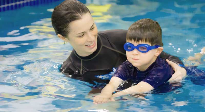 A boy practicing with his swim teacher during a swim lesson