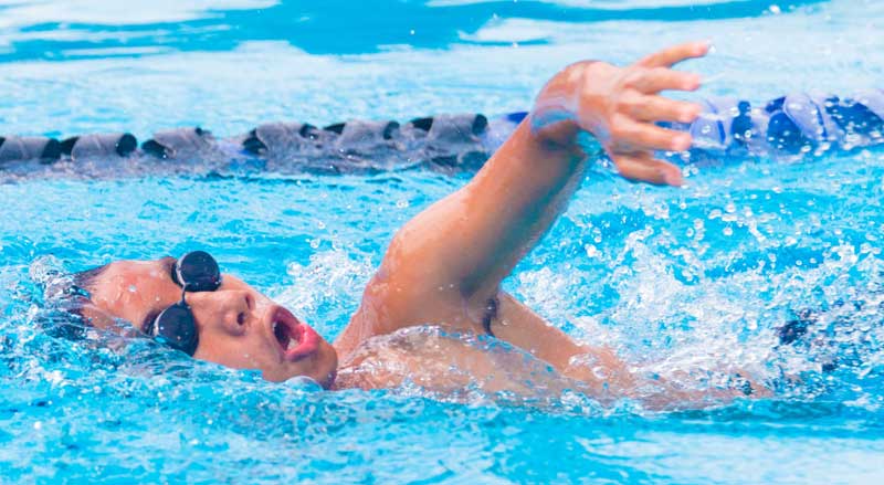 A boy wearing goggles swimming laps in a pool