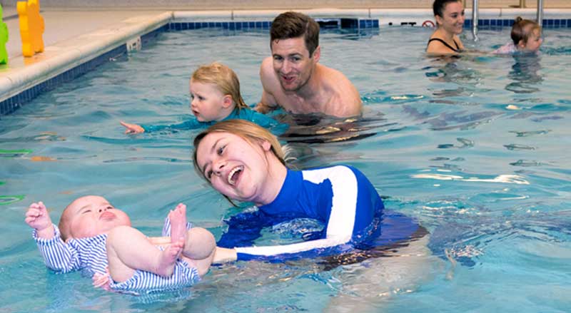 A swim teacher helping an infant float on his back in a pool