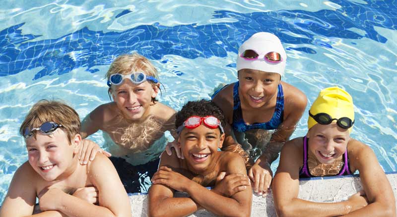 Five kids smiling at the edge of the pool after a swimming lesson.