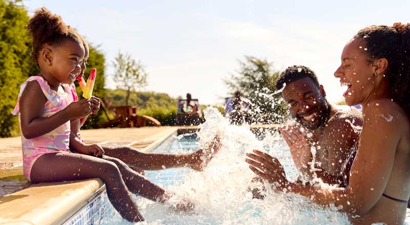 Two happy kids sitting on the side of a pool splashing two adults in the pool