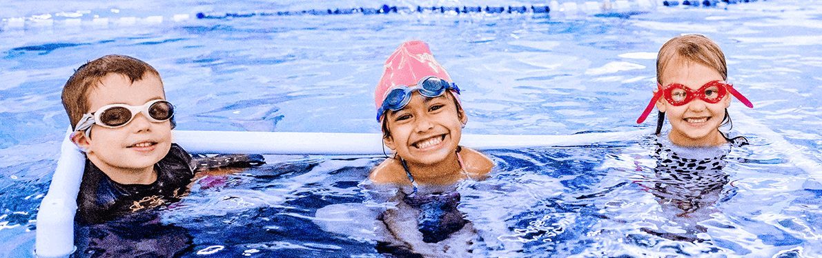 Children participating in a group swim lesson with an instructor in an indoor swimming pool.