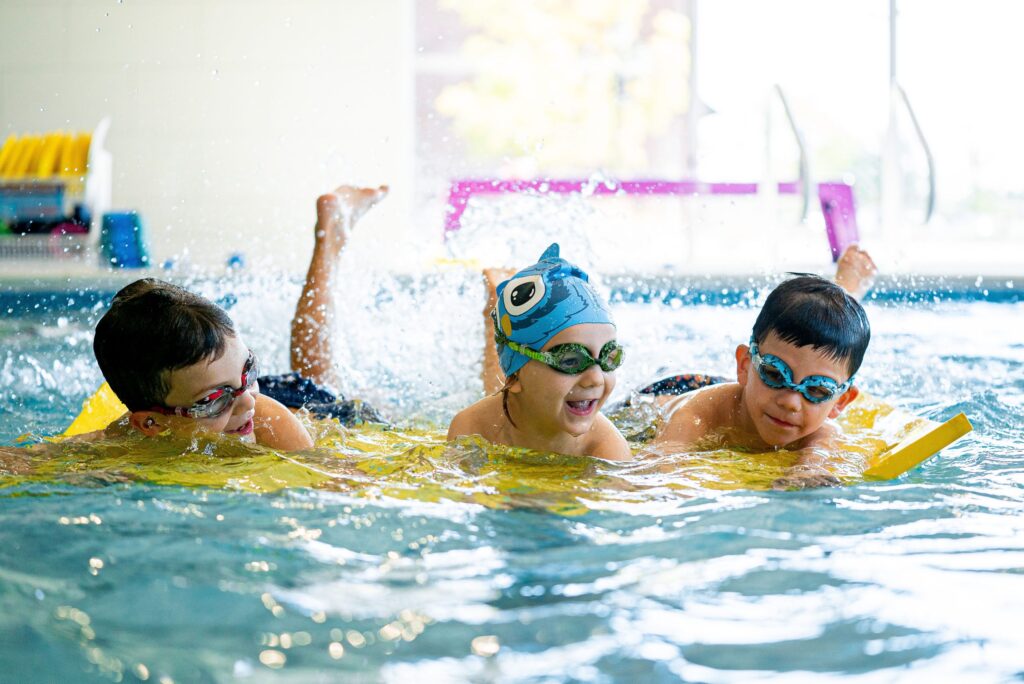 Children participating in a swim lesson with an instructor in an indoor swimming pool.