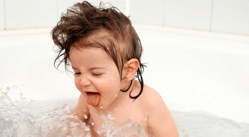 A baby splashing water in a bathtub