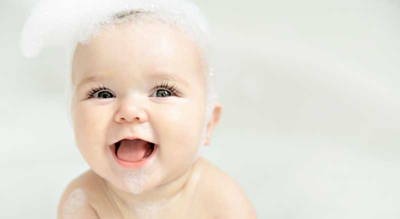 Close-up of smiling baby in a bathtub with shampoo bubbles on her head and chin