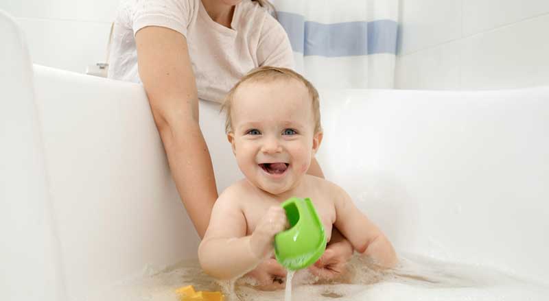 A woman holds baby who is in a bathtub with some toys