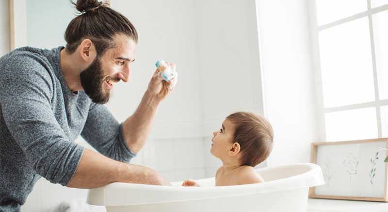 A man playing with a baby while giving him a bath in a baby tub