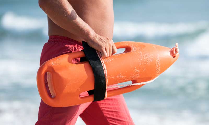 A lifeguard at the beach heading to the water with a floatation device