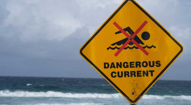 A sign posted in front of the ocean warning beachgoers of a dangerous current
