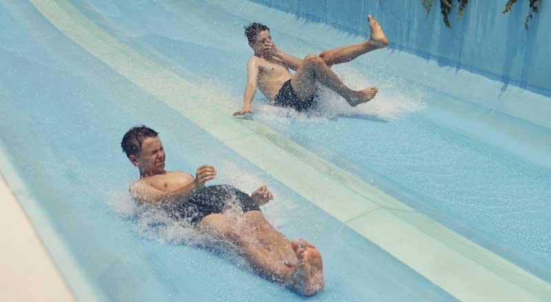 Two boys racing down a water slide in a water park