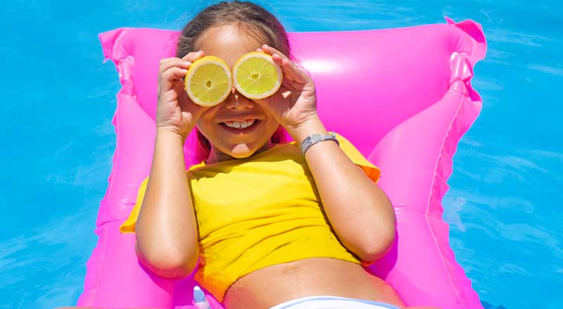 A girl on a bright pink float in a pool in a neon yellow swim top