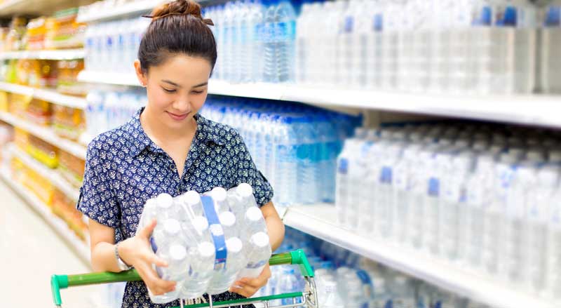 A woman at a grocery store putting water bottles into her shopping cart