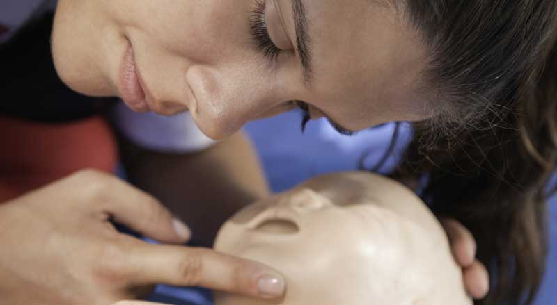 A woman checking breathing on an infant dummy in a CPR class