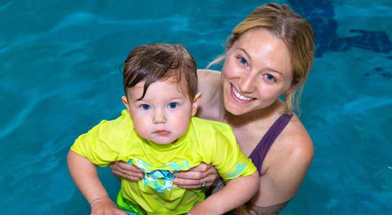A woman supporting a scared child in a swimming pool