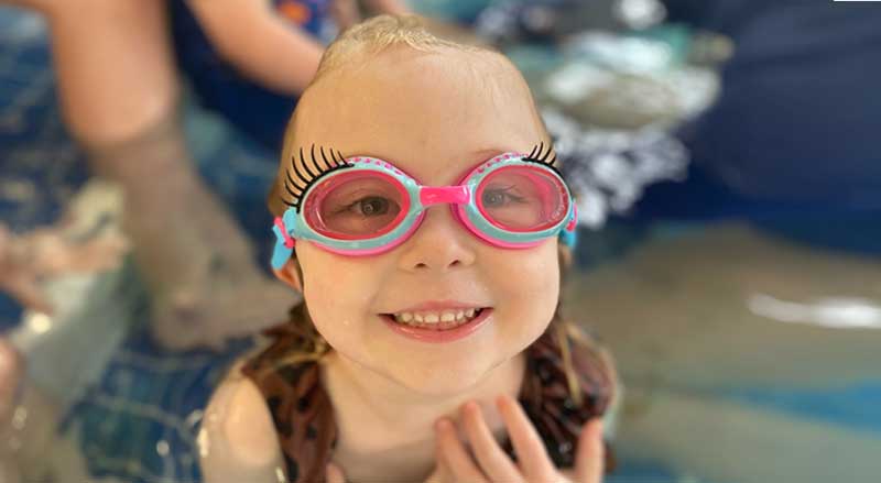 A smiling young girl with funny swim goggles in a pool