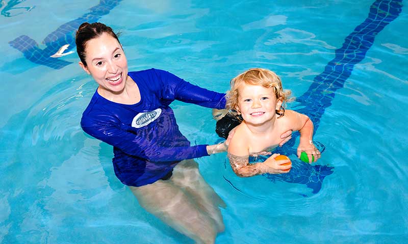 A smiling young swimmer with swim teacher in the water