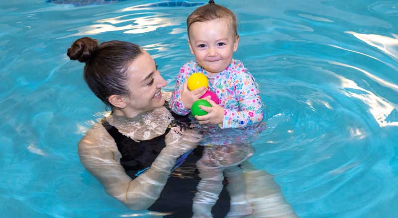 A woman and her toddler playing with toys in a pool