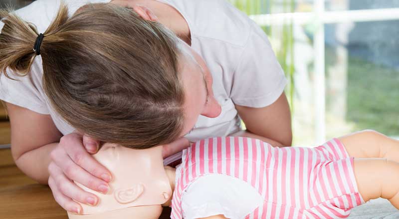 A woman checks an infant dummy for signs of breathing at CPR course