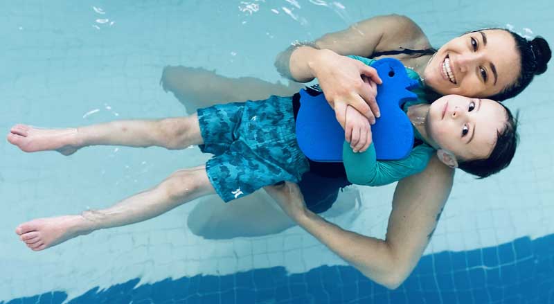 A swimming teacher helps a young boy learn to float in an Njswim School pool