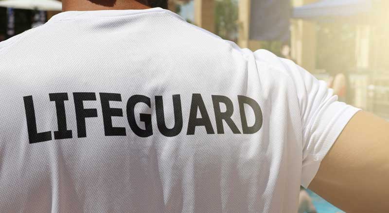 Image of a man wearing a shirt with the words ‘lifeguard’, indicating his role