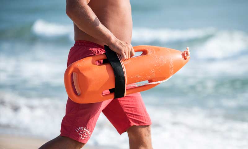 A lifeguard at the beach heading toward water with flotation device