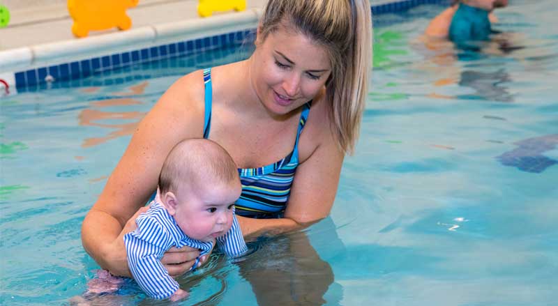 A smiling woman supporting a baby in the pool