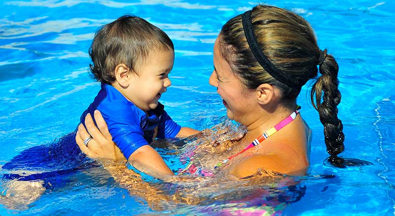 An infant and her mother smiling at each other during a Water Babies swimming class.