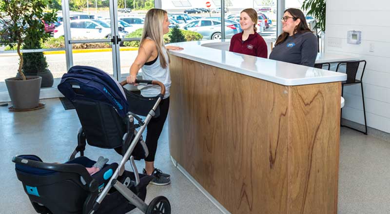 A mother with a stroller talks to two team members at an Njswim school reception desk