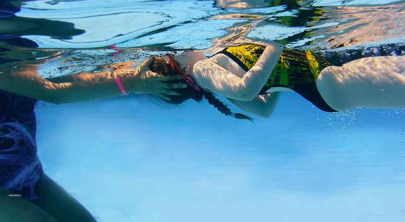 A view from underwater of a swimmer being assisted during swimming lessons from a Njswim teacher