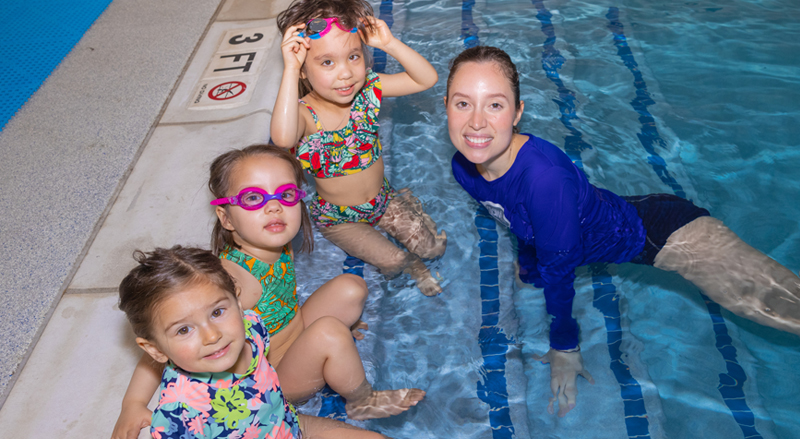 Three kids and their swim teacher in a pool enjoying a swimming lesson