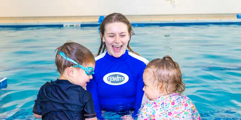 Njswim swim teacher with two very young swimming students in the pool