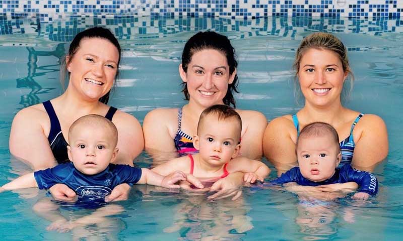 Three moms holding their babies during a water babies swim class