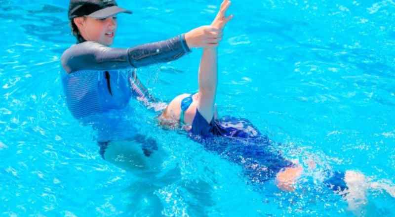 A teacher at Njswim is skillfully guiding a child's arms over their head during their private swimming lesson. 