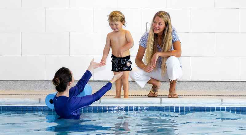 A supportive mother watches proudly as a teacher from Njswim assists him with entering the pool