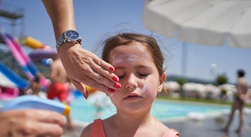 A woman applies sunscreen to young girl’s face