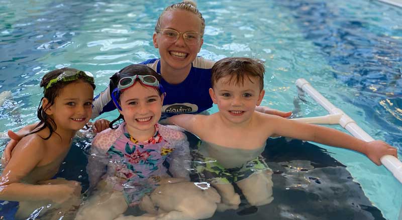 Three smiling kids with their swim teacher in one of the Njswim Schools pools
