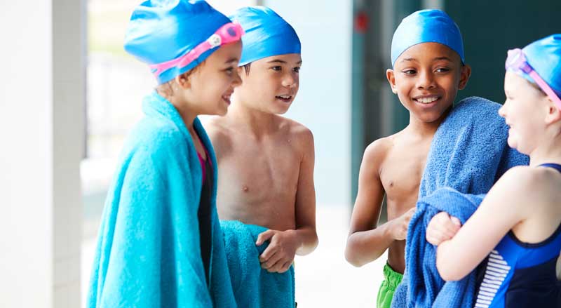 Kids wearing towels socializing with one another after their swim lesson