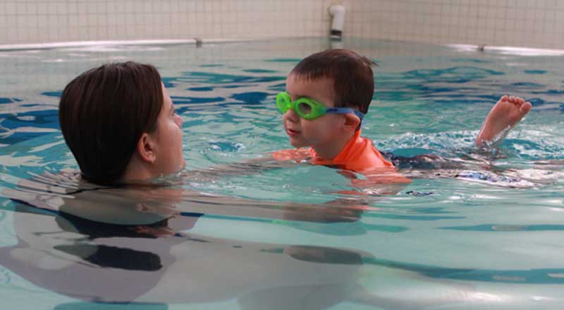 A young child in a pool with his swimming teacher