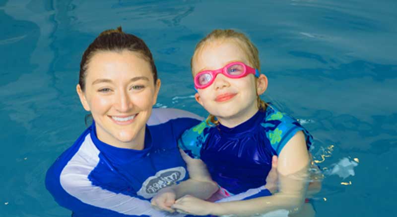 Njswim School teacher in the pool with a young girl wearing pink swim goggles