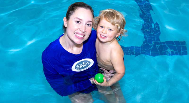 A smiling Njswim instructor supporting a young boy in the pool