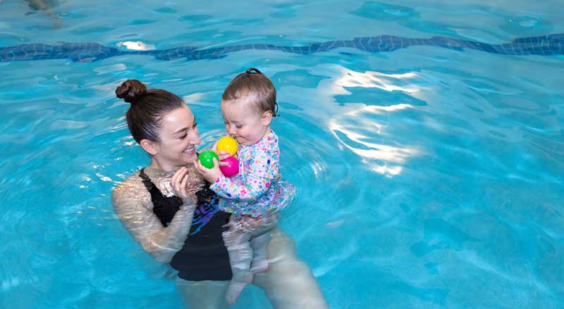 Njswim teacher holding young student in pool