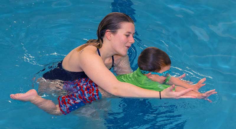 A swim teacher working with a young boy in a swimming class.