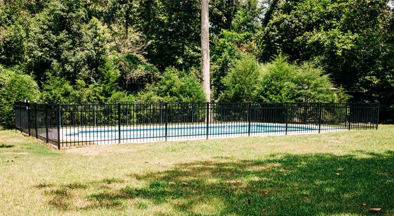 A backyard swimming pool surrounded by a black fence