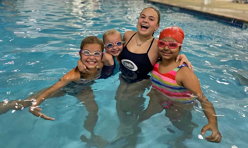 A swim school instructor with three young students in a pool