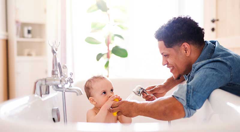 A father bathing his young son in a bathtub